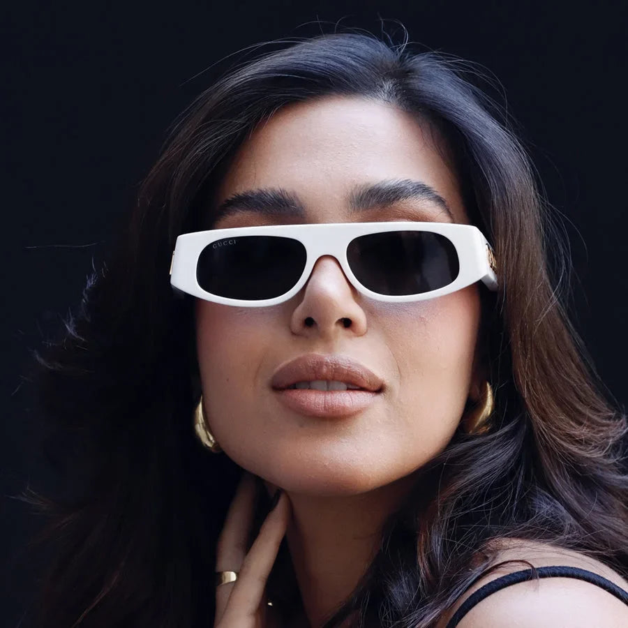 Woman wearing white luxury rectangular sunglasses with dark lenses and gold hoop earrings.
