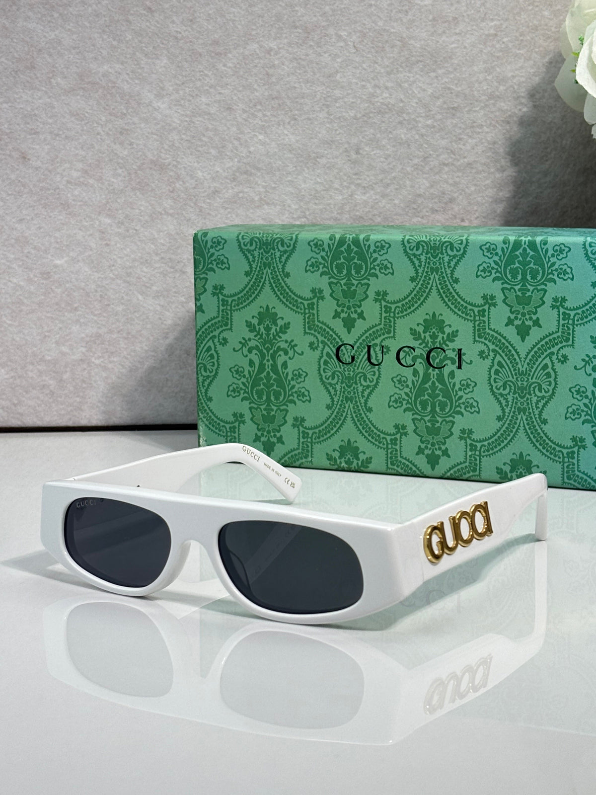 White luxury rectangular sunglasses with gold logo and green patterned Gucci box.